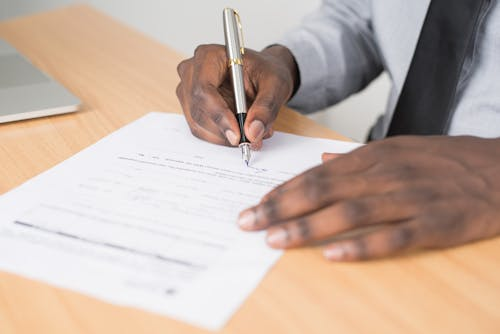 A person holding a pen and paper, illustrating the importance of completing necessary forms when applying for a passport.